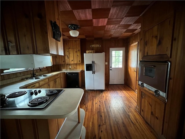 kitchen featuring electric cooktop, wooden walls, white refrigerator with ice dispenser, a sink, and dishwasher