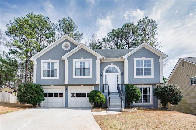 raised ranch featuring driveway, fence, an attached garage, and stucco siding