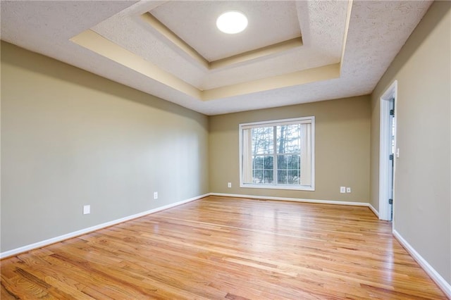 spare room with a raised ceiling, light wood-style flooring, baseboards, and a textured ceiling