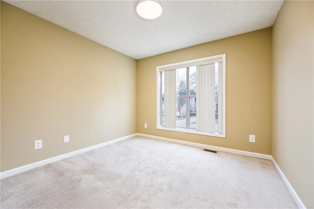 unfurnished room with carpet, a textured ceiling, visible vents, and baseboards