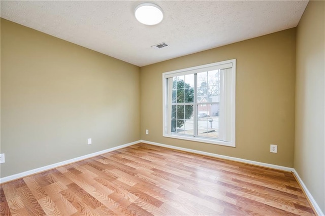 spare room featuring visible vents, light wood-style flooring, baseboards, and a textured ceiling