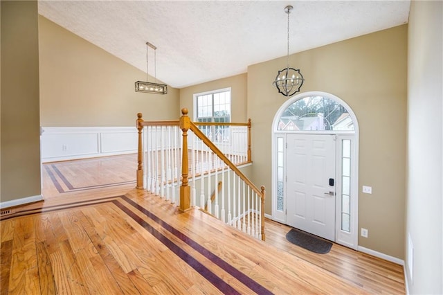 foyer entrance featuring wainscoting, wood finished floors, an inviting chandelier, vaulted ceiling, and a textured ceiling