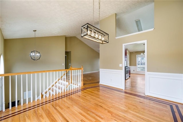 empty room featuring wainscoting, lofted ceiling, wood finished floors, a textured ceiling, and a chandelier