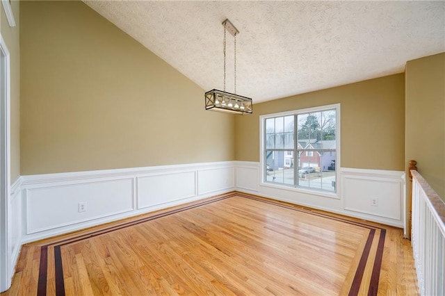 unfurnished dining area with light wood finished floors, wainscoting, lofted ceiling, a textured ceiling, and a notable chandelier