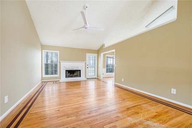 unfurnished living room with lofted ceiling, light wood-type flooring, baseboards, and a ceiling fan