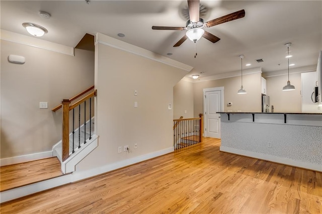 unfurnished living room with crown molding, ceiling fan, and light wood-type flooring