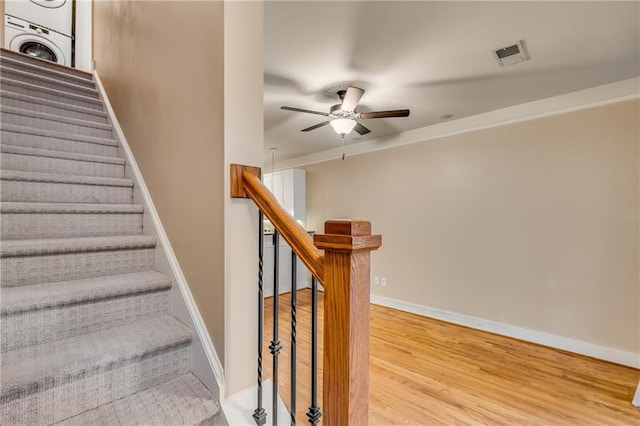 stairway with stacked washer and dryer, hardwood / wood-style floors, and ceiling fan