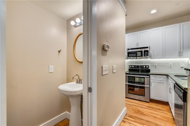 kitchen with white cabinetry, appliances with stainless steel finishes, light wood-type flooring, and decorative backsplash