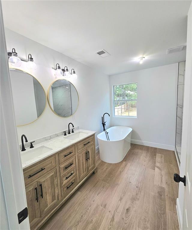 681 Burtons Cv, Hampton, GA 30228 - bathroom with a freestanding bath, wood finished floors, double vanity, and baseboards