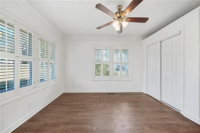 unfurnished bedroom with multiple windows, dark wood finished floors, crown molding, a closet, and ceiling fan