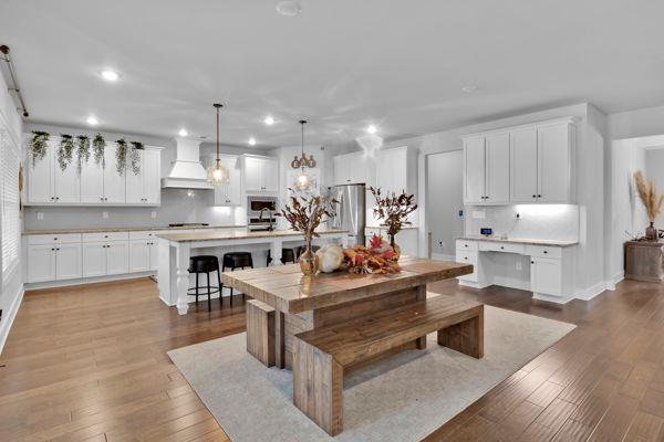 kitchen with white cabinets, pendant lighting, a kitchen island with sink, appliances with stainless steel finishes, and custom range hood