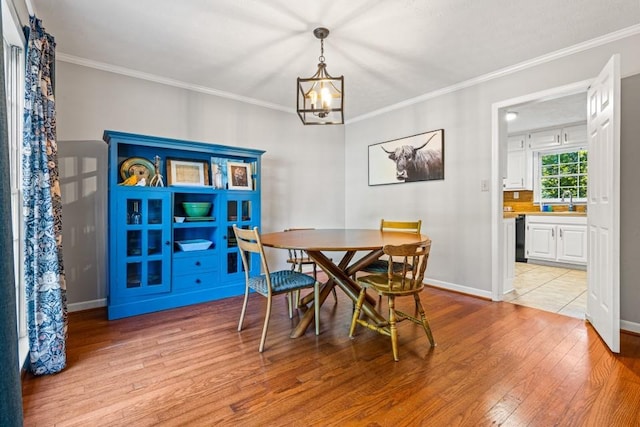 dining room featuring light wood-type flooring, ornamental molding, sink, and a chandelier