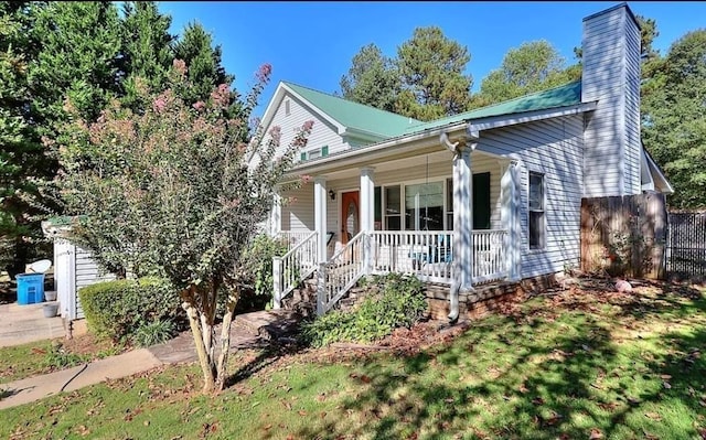 view of front of property with a porch, fence, a chimney, and a front lawn