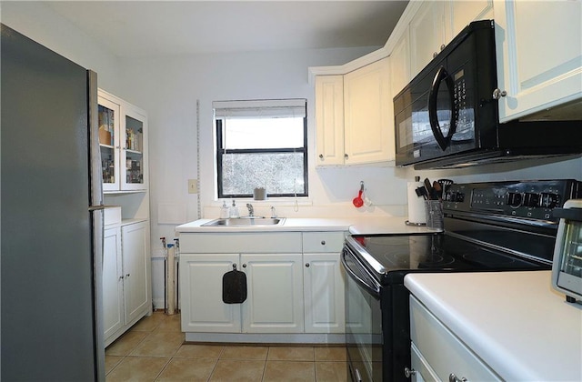 kitchen featuring light tile patterned floors, black appliances, sink, and white cabinets