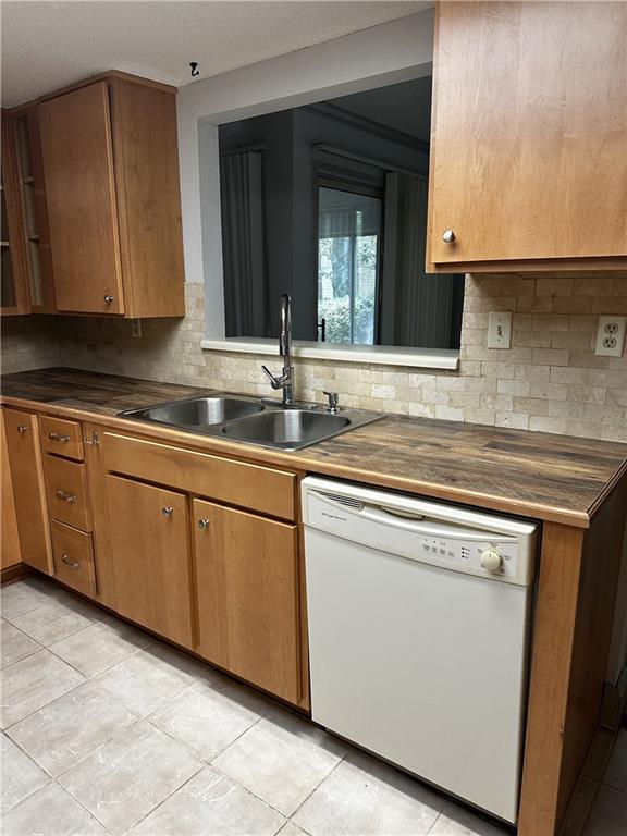 kitchen with backsplash, dishwasher, light tile patterned flooring, and sink