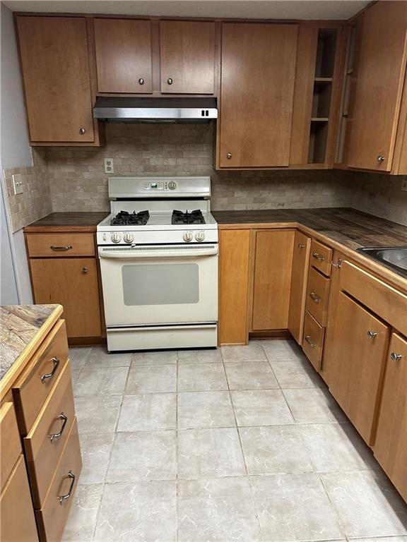 kitchen with backsplash, light tile patterned flooring, sink, and white gas range oven