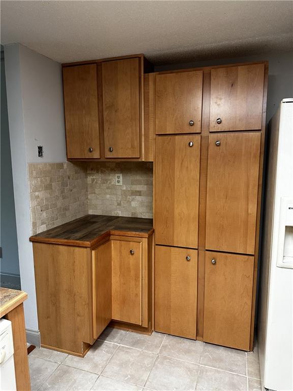 kitchen featuring decorative backsplash, white refrigerator with ice dispenser, a textured ceiling, and light tile patterned floors