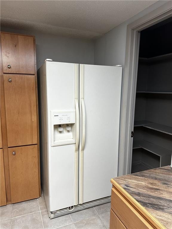 kitchen featuring white fridge with ice dispenser, light tile patterned floors, and a textured ceiling