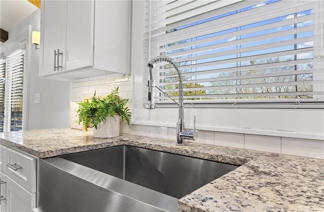 room details with a sink, light stone counters, backsplash, and white cabinets