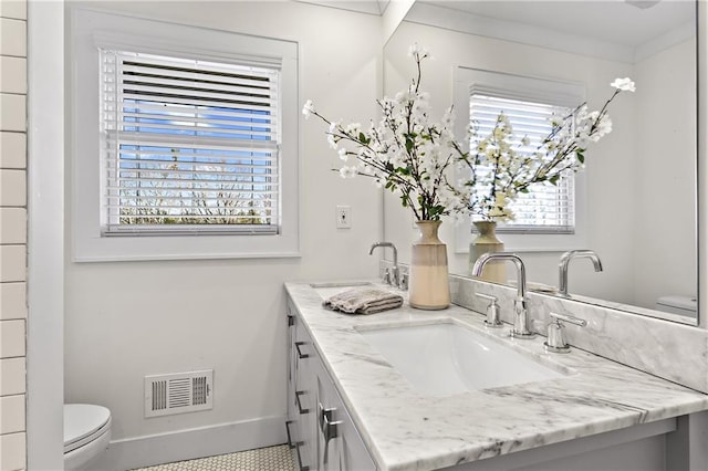 bathroom with double vanity, visible vents, toilet, and a sink