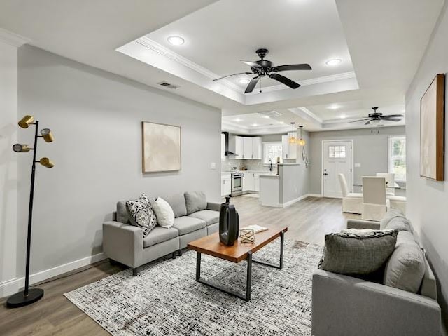 living area featuring baseboards, visible vents, a tray ceiling, crown molding, and light wood-type flooring