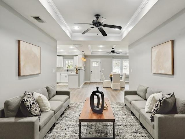 living room featuring visible vents, a raised ceiling, light wood-style floors, and ornamental molding