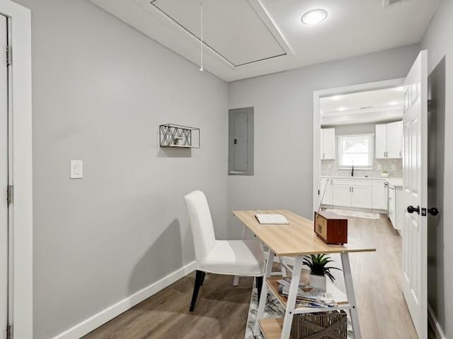 office area with attic access, electric panel, light wood-style floors, and baseboards