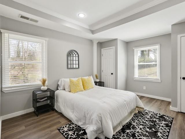 bedroom with visible vents, wood finished floors, baseboards, crown molding, and a raised ceiling