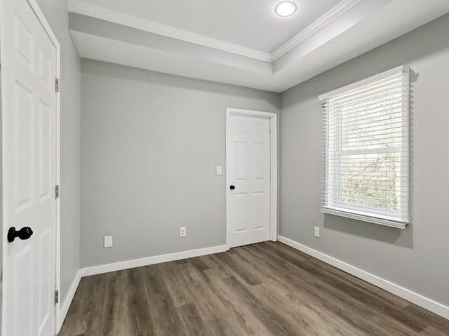 unfurnished bedroom featuring a tray ceiling, baseboards, wood finished floors, and ornamental molding