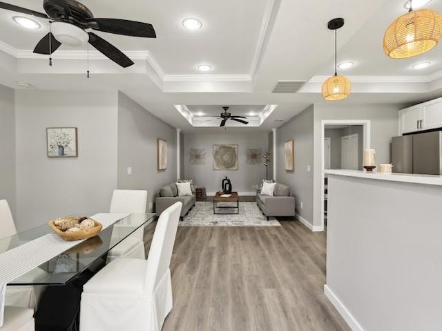 dining area with baseboards, a raised ceiling, light wood-style flooring, and crown molding