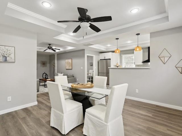 dining area featuring wood finished floors, baseboards, recessed lighting, ornamental molding, and a raised ceiling