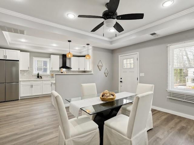 dining space featuring baseboards, light wood finished floors, visible vents, a tray ceiling, and crown molding