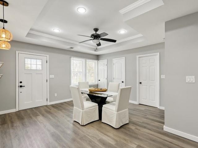 dining room featuring baseboards, a raised ceiling, wood finished floors, and crown molding