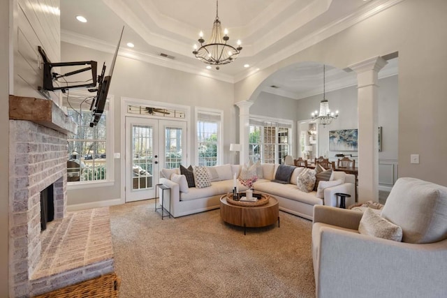 living room with a raised ceiling, a notable chandelier, french doors, and ornate columns