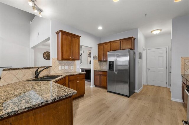 kitchen featuring sink, tasteful backsplash, light hardwood / wood-style flooring, dark stone countertops, and stainless steel fridge