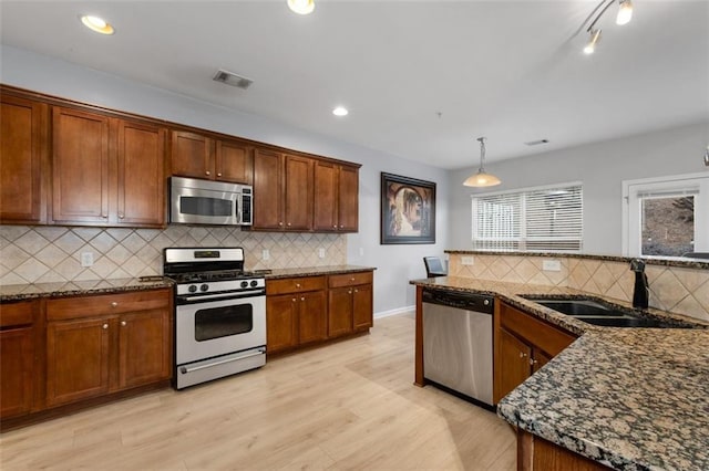 kitchen featuring pendant lighting, sink, appliances with stainless steel finishes, light hardwood / wood-style floors, and dark stone counters