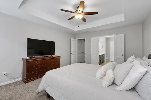 carpeted bedroom with a raised ceiling, connected bathroom, and ceiling fan