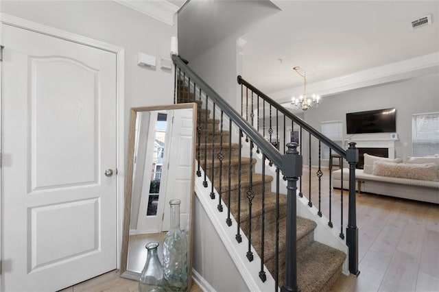 staircase featuring wood-type flooring, ornamental molding, a wealth of natural light, and a chandelier