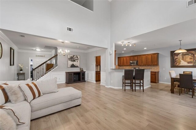 living room featuring an inviting chandelier, crown molding, a towering ceiling, and light wood-type flooring