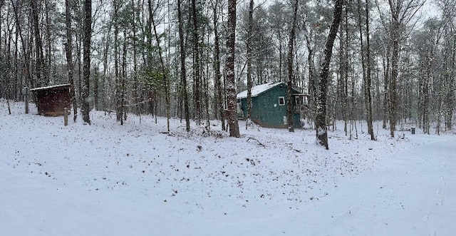 yard covered in snow with an outdoor structure and a wooded view