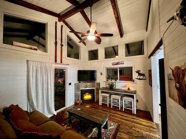 living area featuring lofted ceiling with beams, a ceiling fan, a warm lit fireplace, wood finished floors, and wooden walls