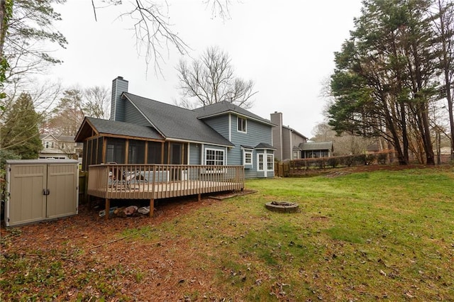 rear view of property featuring a yard, a shed, a wooden deck, an outdoor fire pit, and a sunroom