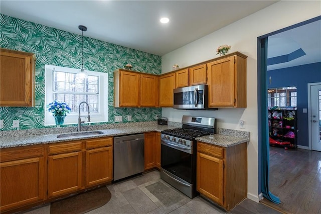 kitchen with sink, stainless steel appliances, pendant lighting, and light stone countertops