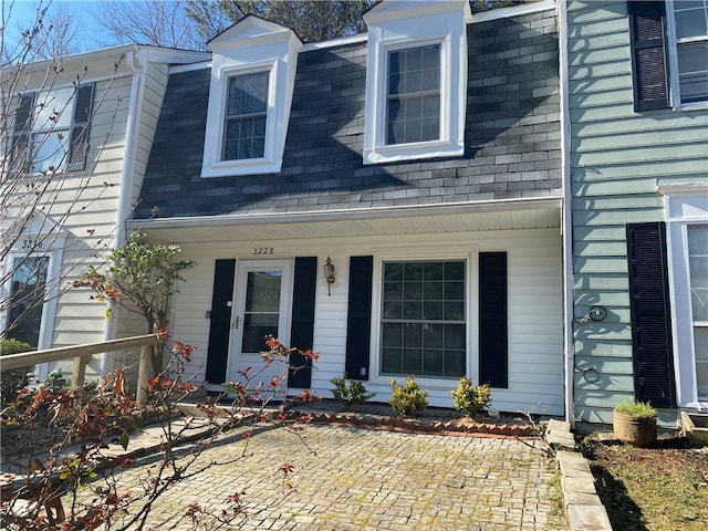 view of exterior entry featuring a shingled roof and covered porch