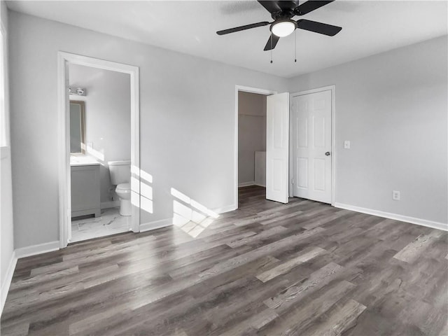 unfurnished bedroom with ensuite bath, a closet, ceiling fan, and dark wood-type flooring