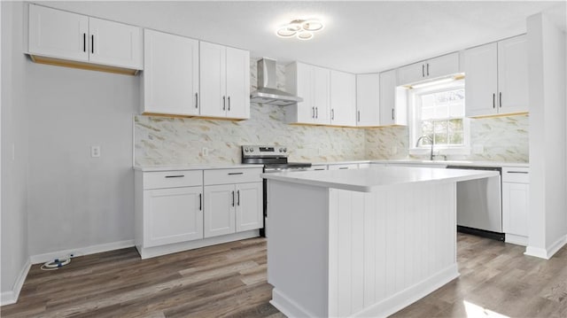 kitchen featuring white cabinets, wall chimney exhaust hood, tasteful backsplash, a kitchen island, and appliances with stainless steel finishes