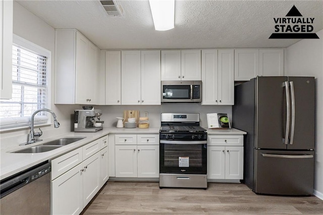 kitchen featuring stainless steel appliances, sink, white cabinets, and light wood-type flooring