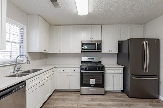 kitchen with stainless steel appliances, sink, white cabinets, and light wood-type flooring