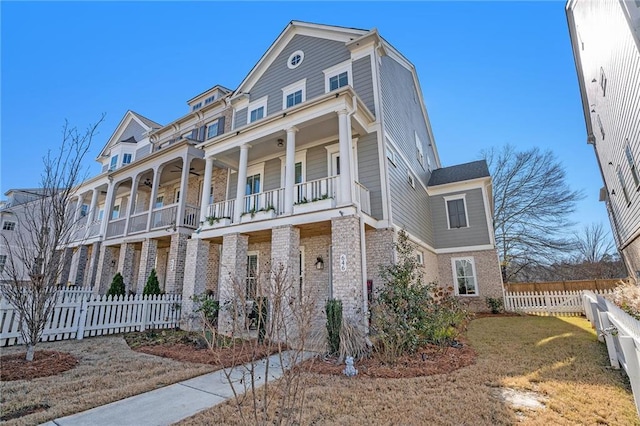 view of front of house featuring brick siding, ceiling fan, a balcony, and fence