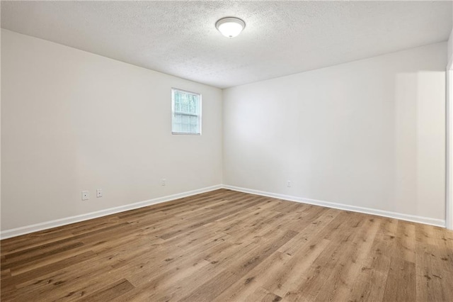 unfurnished room with a textured ceiling, baseboards, and wood finished floors